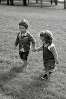 Two young children joyfully holding hands and walking in a grassy field, captured in charming black and white.