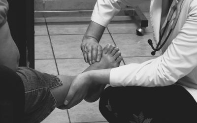 Doctor examines a patient's foot during a medical consultation in a clinic setting.